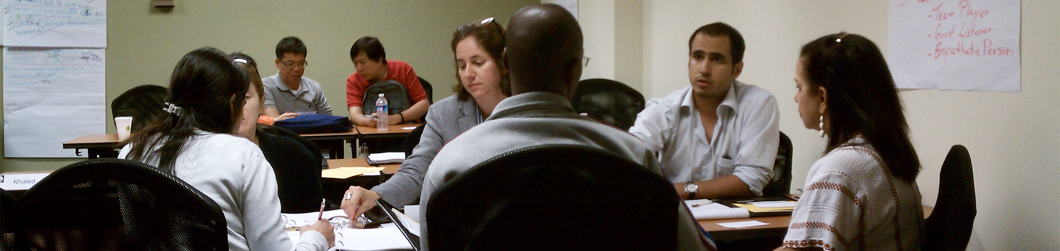 Conference participants sit together at long tables and hold a discussion.