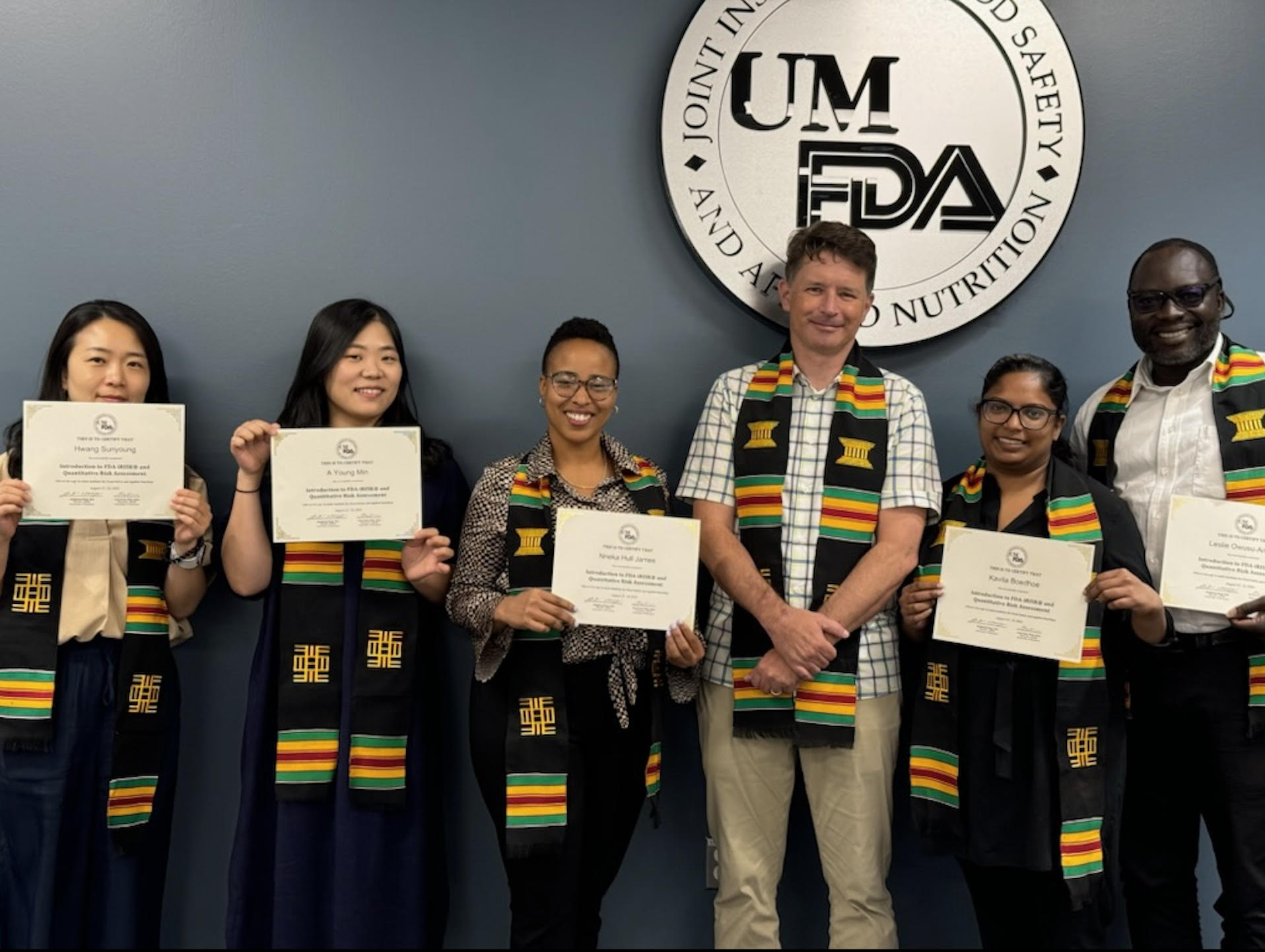 Greg Paoli and class participants holding certificates stand for a group photo in front of the JIFSAN logo.